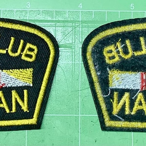 May include: Two black embroidered patches with yellow trim. One patch reads "STRIP CLUB VETERAN" in yellow thread. The other patch is a mirror image of the first. Both patches have a central design with blue, red, and yellow details.