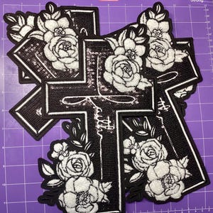 May include: Black cross-shaped patches with white floral designs and the word "faith" in script. The patches have a sequined texture and a white border. The floral elements include roses and leaves.