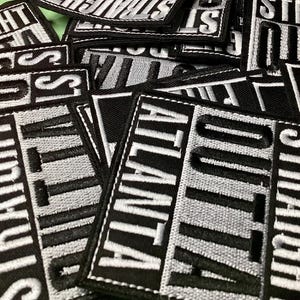 May include: A collection of black and white embroidered patches. Each patch is rectangular and features the words "Straight Outta Atlanta" in a bold, blocky font. The text is in white, with a black border.