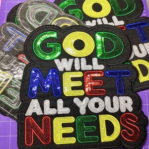 May include: Black fabric patches with the message "GOD WILL MEET ALL YOUR NEEDS" in colorful sequined letters. The patches have a black border and are arranged on a purple surface. The letters are in green, yellow, blue, red, and white.