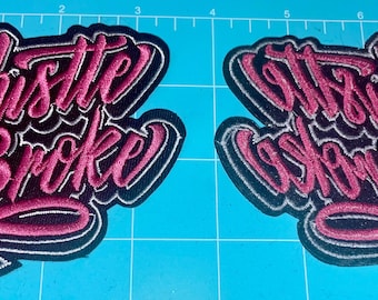 May include: Two embroidered patches with the phrases "Hustle or Be Broke" and "It's Built, Not Bought" in a cursive font. The patches have a black background with pink and white lettering.