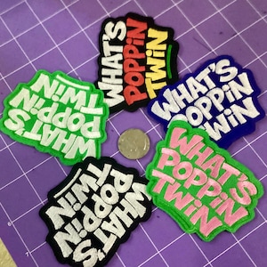 Puede incluir: Cinco parches bordados con el texto "WHAT'S POPPIN TWIN" en varias combinaciones de colores. Los parches incluyen texto blanco sobre verde, texto rojo y amarillo sobre negro, texto blanco sobre azul, texto blanco sobre negro y texto rosa sobre verde.