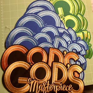Può includere: Toppe ricamate in vari colori. Le toppe includono le parole "GOD'S Masterpiece" in oro e arancione, insieme a disegni ad arco blu e verdi. Le toppe sono disposte su un tappetino da taglio verde.