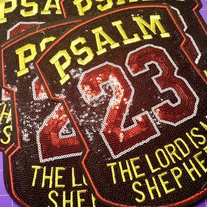 May include: Black and red sequined patch with the text "PSALM 23" and "THE LORD IS SHEPHERD" in yellow. The patch has a shield shape with a white border and is likely for apparel or crafts.