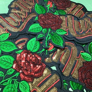 May include: Multiple embroidered patches featuring the word Hustle in gold sequins with red outlines. Each patch includes detailed red sequined roses and vibrant green embroidered leaves on a black fabric base, arranged in a layered composition.