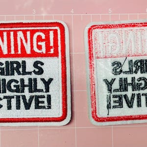 Può includere: Due toppe rettangolari con bordi rossi e sfondi bianchi. Le toppe recitano "WARNING! BIG GIRLS ARE HIGHLY ADDICTIVE!" in testo nero. Una toppa è a testa in su e l'altra è capovolta.