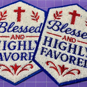 May include: Two white, hexagonal embroidered patches with blue borders. Each patch features the words "Blessed AND HIGHLY FAVORED" in blue script, a red cross, and red floral accents.