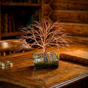 Puede incluir: Una escultura decorativa de &aacute;rbol hecha de alambre de cobre fino y retorcido. El &aacute;rbol presenta una copa ancha y extendida de finas ramas de alambre y est&aacute; anclado a una base rectangular texturizada que parece un trozo de madera oscura y musgosa.