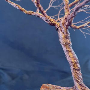 Puede incluir: Una escultura de &aacute;rbol hecha de alambre de cobre trenzado, con un tronco grueso y entrelazado que se ramifica en numerosas ramas finas y delicadas. El metal tiene un acabado c&aacute;lido e iridiscente con tonos bronce, dorados y p&uacute;rpuras.