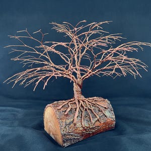 Puede incluir: Una escultura decorativa que presenta un &aacute;rbol de alambre de cobre con ramas finas e intrincadas que se extienden hacia afuera. El &aacute;rbol est&aacute; anclado en una base de tronco de madera natural y cil&iacute;ndrica, con ra&iacute;ces de cobre sobre la corteza.