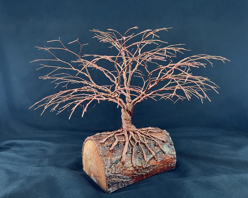 Puede incluir: Una escultura decorativa que presenta un &aacute;rbol de alambre de cobre con ramas finas e intrincadas que se extienden hacia afuera. El &aacute;rbol est&aacute; anclado en una base de tronco de madera natural y cil&iacute;ndrica, con ra&iacute;ces de cobre sobre la corteza.