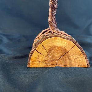 Puede incluir: Una escultura decorativa con una base de madera semicircular con vetas y bordes de corteza visibles. Una estructura de alambre trenzado de color marr&oacute;n oscuro se extiende hacia arriba desde el centro de la parte superior plana de la madera.