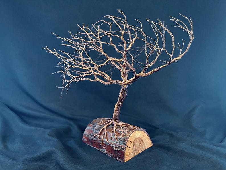 Puede incluir: Una escultura de &aacute;rbol hecha de alambre de color cobre trenzado, con ramas intrincadas que se extienden hacia afuera. El tronco y las ra&iacute;ces de alambre est&aacute;n anclados en una pieza de madera natural semicil&iacute;ndrica con corteza y veta.