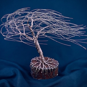 Puede incluir: Una escultura de &aacute;rbol hecha de alambre de cobre fino, con un tronco retorcido y largas ramas que se extienden hacia un lado. Las ra&iacute;ces de alambre est&aacute;n ancladas en una base de madera circular de color marr&oacute;n oscuro con acabado rugoso.