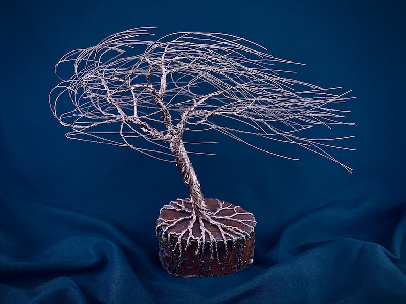 Puede incluir: Una escultura de &aacute;rbol hecha de alambre de cobre fino, con un tronco retorcido y largas ramas que se extienden hacia un lado. Las ra&iacute;ces de alambre est&aacute;n ancladas en una base de madera circular de color marr&oacute;n oscuro con acabado rugoso.