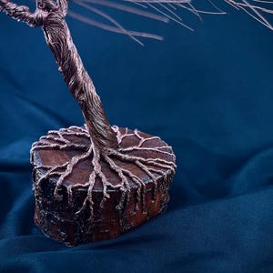Puede incluir: Una escultura decorativa de &aacute;rbol hecha de alambre de cobre trenzado. El tronco y las ramas se extienden hacia arriba, mientras que las ra&iacute;ces de alambre se extienden sobre la superficie superior de una base de madera redonda y marr&oacute;n.