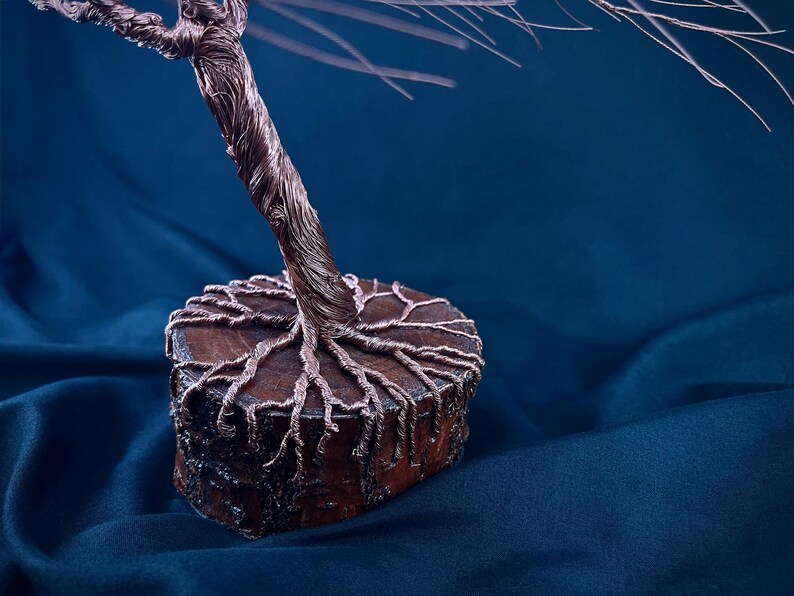 Puede incluir: Una escultura decorativa de &aacute;rbol hecha de alambre de cobre trenzado. El tronco y las ramas se extienden hacia arriba, mientras que las ra&iacute;ces de alambre se extienden sobre la superficie superior de una base de madera redonda y marr&oacute;n.
