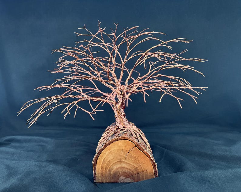 Puede incluir: Una escultura de &aacute;rbol hecha de alambre de cobre fino, con ramas intrincadas que se extienden hacia afuera. La base del &aacute;rbol est&aacute; formada por una pieza de madera natural semicil&iacute;ndrica, que muestra vetas visibles y corteza en el exterior.