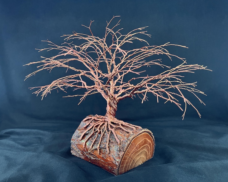 Puede incluir: Una escultura decorativa de &aacute;rbol hecha de alambre de cobre trenzado. El &aacute;rbol presenta una red compleja de ramas delgadas y un tronco grueso y trenzado. La base es un tronco de madera cil&iacute;ndrico con corteza y veta visibles.