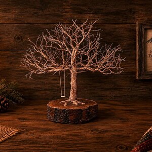 May include: A wire sculpture of a bare tree with a small swing hanging from a branch, mounted on a circular wooden base. The tree features intricate, twisted metallic branches and a textured trunk, creating a detailed, sculptural representation of a tree.