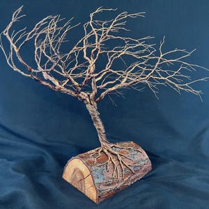 Puede incluir: Una escultura de &aacute;rbol con un tronco met&aacute;lico retorcido y ramas intrincadas y extendidas. El &aacute;rbol est&aacute; anclado a una pieza de madera natural semicil&iacute;ndrica que sirve de base, con ra&iacute;ces met&aacute;licas que se extienden sobre la superficie.