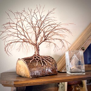 Puede incluir: Una escultura de alambre de un &aacute;rbol sin hojas con ramas y ra&iacute;ces de color cobre unidas a una base de tronco de madera natural. El &aacute;rbol presenta detalles intrincados de alambre trenzado que imitan un &aacute;rbol desnudo.