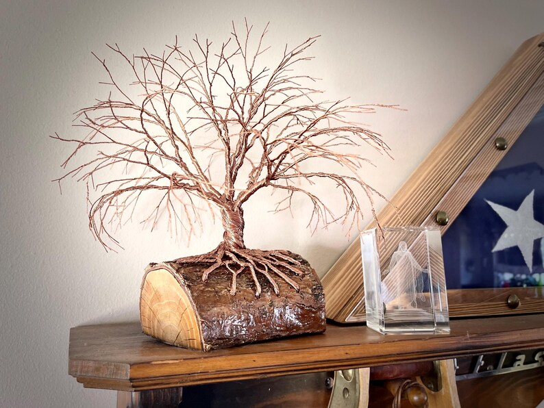Puede incluir: Una escultura de alambre de un &aacute;rbol sin hojas con ramas y ra&iacute;ces de color cobre unidas a una base de tronco de madera natural. El &aacute;rbol presenta detalles intrincados de alambre trenzado que imitan un &aacute;rbol desnudo.