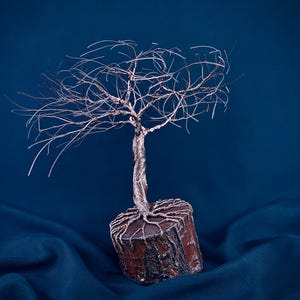 Puede incluir: Una escultura decorativa de &aacute;rbol hecha de alambre fino y retorcido de color cobre. Las ramas de alambre se extienden hacia afuera desde un tronco central anclado en una base cil&iacute;ndrica de madera con textura de corteza y ra&iacute;ces visibles.