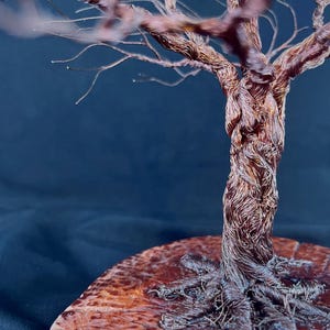 May include: A decorative sculpture of a tree crafted from twisted copper wire. The trunk and branches are formed by numerous thin, metallic strands. The tree is mounted on a circular, polished wooden base with a visible grain and textured surface.