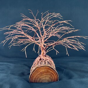 Puede incluir: Una escultura decorativa que presenta un &aacute;rbol de alambre de cobre con ramas finas e intrincadas que se extienden hacia afuera. La base del &aacute;rbol est&aacute; formada por ra&iacute;ces de alambre de cobre envueltas alrededor de un cilindro de madera natural.