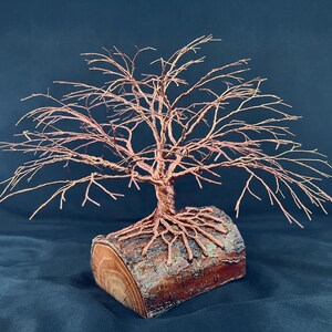 Puede incluir: Una escultura de &aacute;rbol hecha de alambre de cobre trenzado, con ramas intrincadas y ra&iacute;ces expuestas. El &aacute;rbol de alambre est&aacute; montado de forma segura sobre una base de tronco de madera natural y cil&iacute;ndrica con textura de corteza visible.