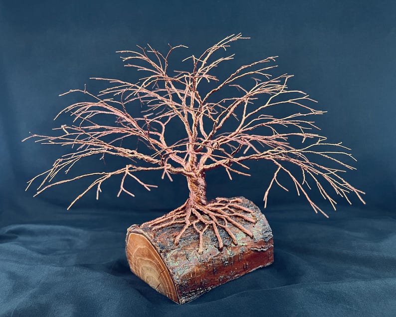 Puede incluir: Una escultura de &aacute;rbol hecha de alambre de cobre trenzado, con ramas intrincadas y ra&iacute;ces expuestas. El &aacute;rbol de alambre est&aacute; montado de forma segura sobre una base de tronco de madera natural y cil&iacute;ndrica con textura de corteza visible.