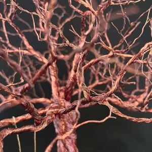 May include: A sculpture of a tree crafted from thin, metallic copper wire. The structure features a central trunk that branches out into numerous fine, twisted wire limbs, mimicking the appearance of bare tree branches in a dense, intricate network.