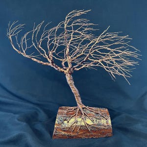 Puede incluir: Una escultura de un &aacute;rbol azotado por el viento hecha de alambre de color cobre retorcido. El &aacute;rbol presenta una red densa de ramas delgadas que se extienden hacia un lado y est&aacute; anclado en una pieza rectangular de madera natural con corteza.