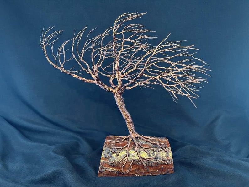 Puede incluir: Una escultura de un &aacute;rbol azotado por el viento hecha de alambre de color cobre retorcido. El &aacute;rbol presenta una red densa de ramas delgadas que se extienden hacia un lado y est&aacute; anclado en una pieza rectangular de madera natural con corteza.