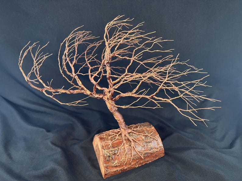 Puede incluir: Una escultura de &aacute;rbol hecha de alambre de cobre trenzado, con ramas intrincadas que se extienden hacia afuera. La base del &aacute;rbol est&aacute; anclada en una pieza cil&iacute;ndrica de madera natural con corteza visible, mostrando las ra&iacute;ces de alambre integradas.