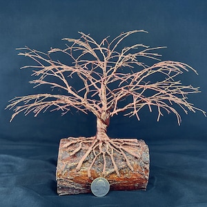 Puede incluir: Una escultura de alambre de cobre de un &aacute;rbol con ramas intrincadas y ra&iacute;ces expuestas envueltas alrededor de una base de tronco de madera cil&iacute;ndrica. Una moneda est&aacute; colocada en la base para dar escala, midiendo 24,26 mil&iacute;metros de di&aacute;metro.