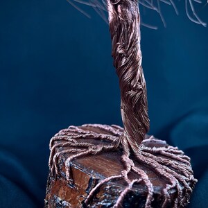 Puede incluir: Una escultura decorativa de &aacute;rbol hecha de alambre de cobre trenzado. El tronco y las ra&iacute;ces expuestas est&aacute;n formados por haces de alambre de cobre met&aacute;lico, con las ra&iacute;ces extendi&eacute;ndose sobre la superficie superior de una base de madera.