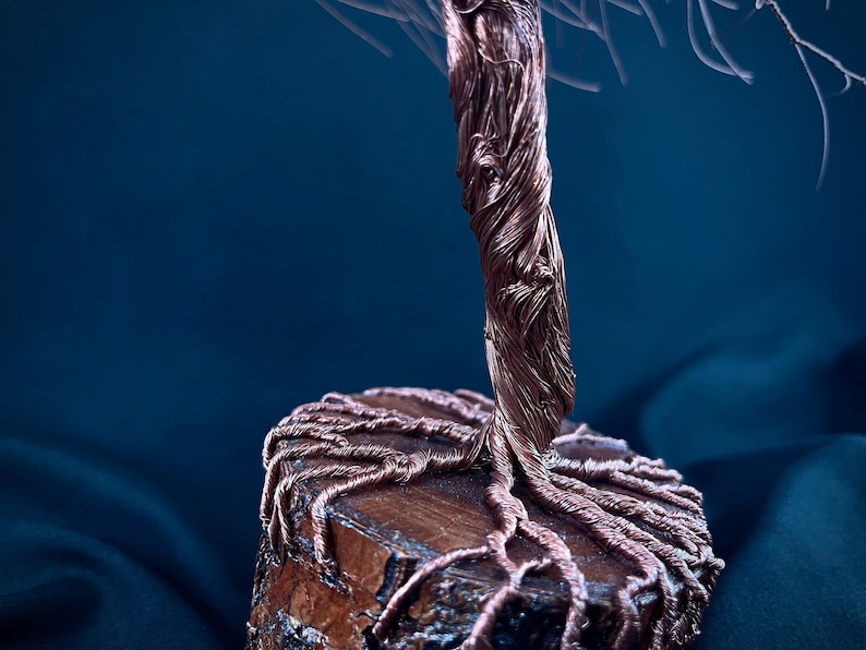Puede incluir: Una escultura decorativa de &aacute;rbol hecha de alambre de cobre trenzado. El tronco y las ra&iacute;ces expuestas est&aacute;n formados por haces de alambre de cobre met&aacute;lico, con las ra&iacute;ces extendi&eacute;ndose sobre la superficie superior de una base de madera.