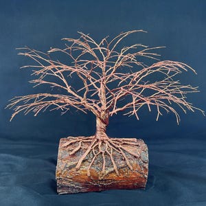 Puede incluir: Una escultura decorativa de &aacute;rbol hecha de alambre de cobre trenzado. El &aacute;rbol presenta una copa ancha y extendida de ramas finas y desnudas, y un tronco grueso y trenzado que se extiende en estructuras similares a ra&iacute;ces ancladas en un tronco.