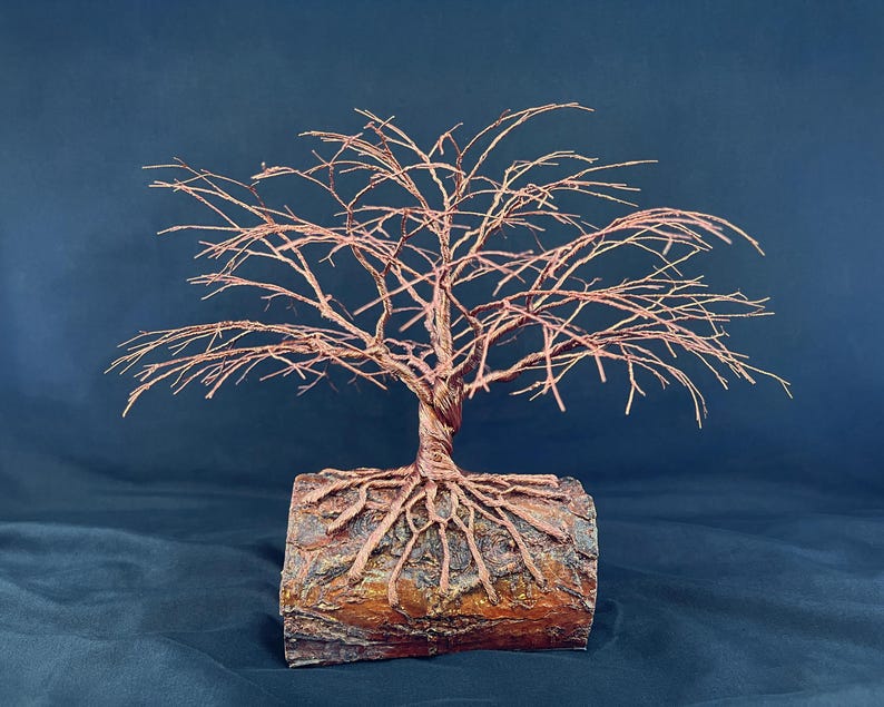 Puede incluir: Una escultura decorativa de &aacute;rbol hecha de alambre de cobre trenzado. El &aacute;rbol presenta una copa ancha y extendida de ramas finas y desnudas, y un tronco grueso y trenzado que se extiende en estructuras similares a ra&iacute;ces ancladas en un tronco.