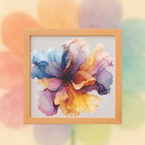 Puede incluir: Un punto de cruz enmarcado de una flor colorida. La flor presenta tonos de azul, morado, amarillo y naranja. El marco de madera es de color marrón claro. El fondo es un diseño de acuarela suave y borroso.