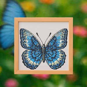Op de afbeelding: Een ingelijste kruissteek van een blauwe vlinder met ingewikkelde vleugelpatronen. De vlinder is gecentreerd in een licht houten frame, tegen een vage groene en roze bloemenachtergrond. De vleugels van de vlinder hebben tinten blauw en wit.