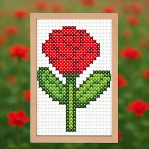 Könnte beinhalten: Ein gerahmtes Kreuzstichbild einer roten Rose mit grünen Blättern und Stiel. Die Blume ist auf einem weißen Hintergrund zentriert, und der Rahmen ist hellbraun. Der Hintergrund ist ein verschwommenes Feld roter Blumen.