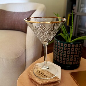 Op de afbeelding: Een helder kristallen martini glas met een gouden rand en de gegraveerde tekst "The Millers". Het glas staat op een houten en marmeren onderzetter met de tekst "SCHAEVE" en "Est. May 2015".