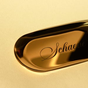 Close-up of gold minimalist oval catch-all tray showcasing smooth metallic surface and clean edges, styled with rings and small jewelry.