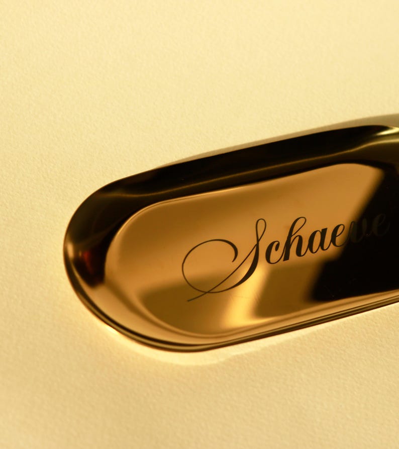 Close-up of gold minimalist oval catch-all tray showcasing smooth metallic surface and clean edges, styled with rings and small jewelry.