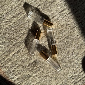 May include: Four rectangular clear glass perfume bottles with gold-colored metal caps. Each bottle features a slender, elongated shape and a transparent body. The bottles are arranged in a scattered formation, reflecting light and casting distinct shadows.