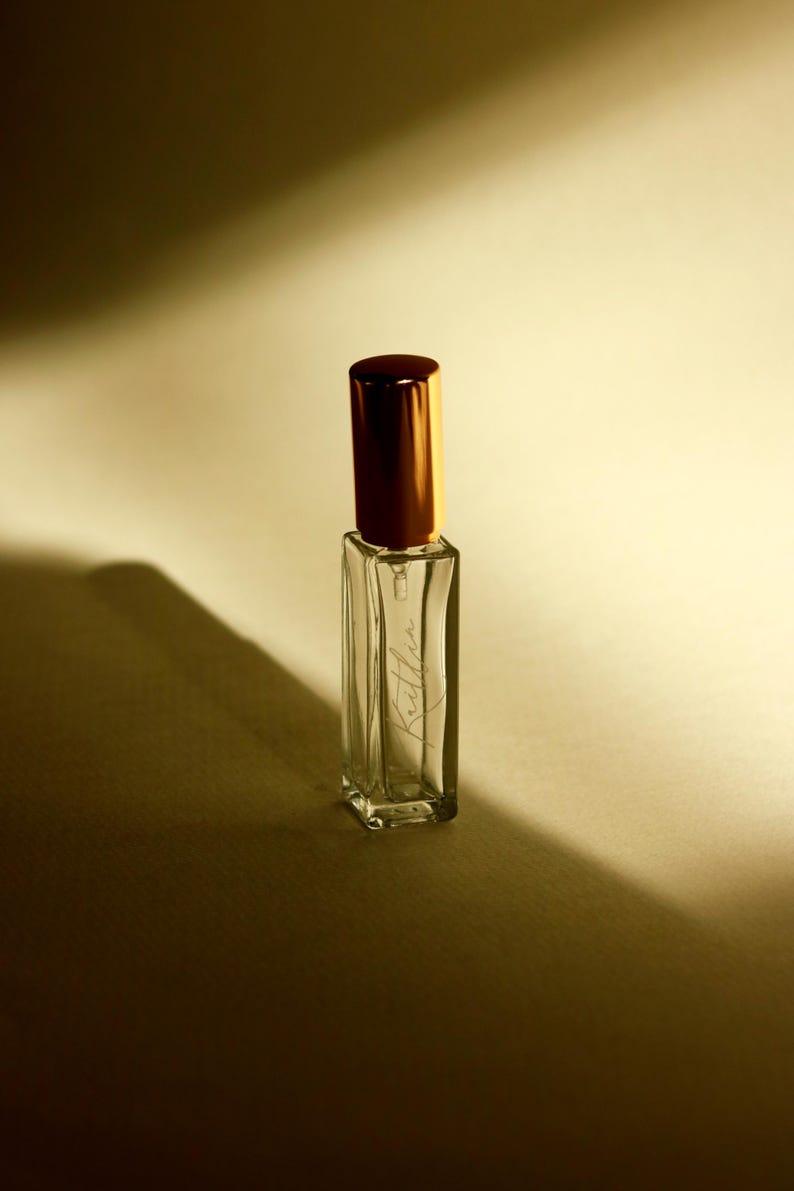 May include: A clear, rectangular glass perfume bottle with a metallic gold cylindrical cap. The front of the bottle features the name Kaitlin written in a delicate, cursive script. The bottle is empty and stands upright with sharp, defined edges.