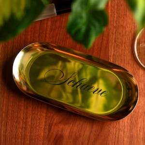 Silver metal oval trinket tray on light tabletop, modern minimalist design used as jewelry dish and vanity organizer.